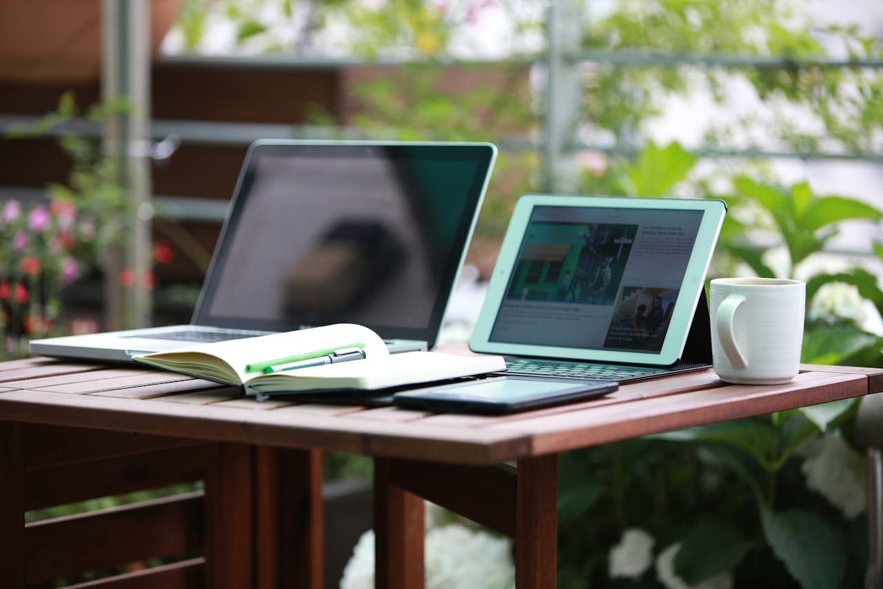 A cozy outdoor workspace scene with a laptop, tablet, and mug on a wooden table.