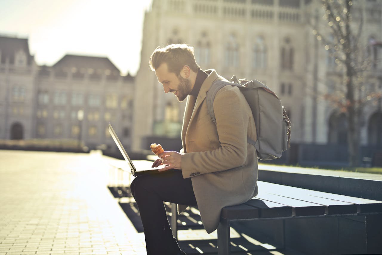 Man working on laptop in Budapest park while enjoying ice cream, showcasing remote work lifestyle.
